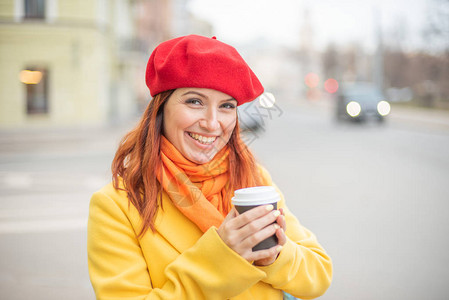 穿着黄色外套和红色贝雷帽的红发年轻女子正在街上喝咖啡取暖一个穿着鲜艳外衣的女孩高图片