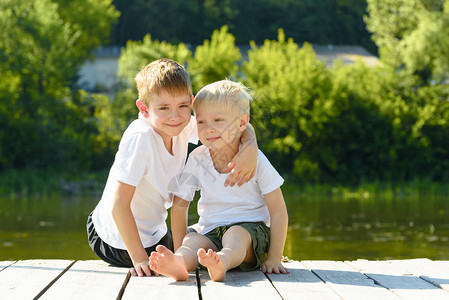 两个小男孩坐在河岸的怀抱中友谊和博爱的理念图片