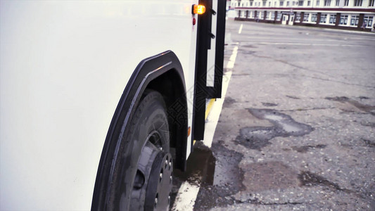 在灰色沥青背景上打开门和公共汽车轮的白色公共汽车的侧视图客车特写开门闪光灯及其轮子商业图片