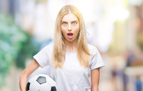年轻漂亮的金发女子在与世隔绝的背景下举着足球图片