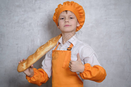 一个穿着橙色厨服的可爱男孩拿着一个面包卷并展示了类似手势图片