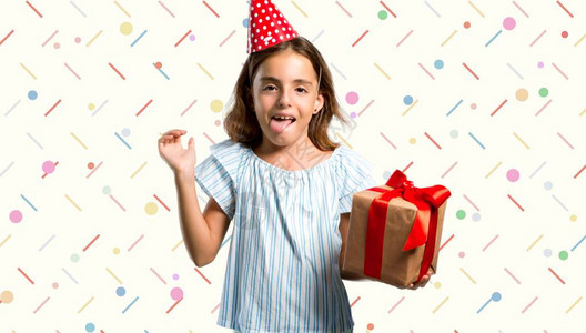 有个小女孩在生日派对上拿着礼物的小女孩在摄影机前放舌头笑背景图片