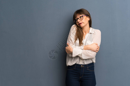 蓝色墙上戴眼镜的女人在抬起肩膀时作图片