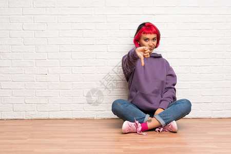 穿着粉色头发坐在地板上的年轻女人用负面的表情图片