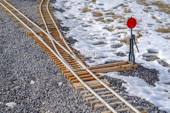 铁路在多岩石的地面上结雪两条铁路会聚或分叉的铁路枢纽的特写视图在白雪覆盖的岩石地面上可以看到一个红图片