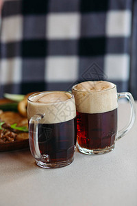 两个装满泡沫冰镇啤酒的大玻璃杯站在餐厅或酒吧的光滑桌面上图片