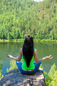 在山顶上做瑜伽坐在森林中的一块自然岩石上露托斯的姿势图片