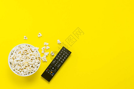 一碗爆米花和黄色背景上的电视遥控器图片