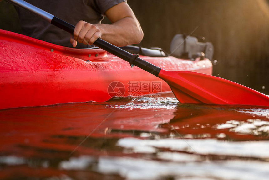 在湖上用划桨在红皮艇上划船的男子图片