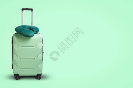 绿色背景上的塑料手提箱和旅行枕头旅行商务旅行探图片
