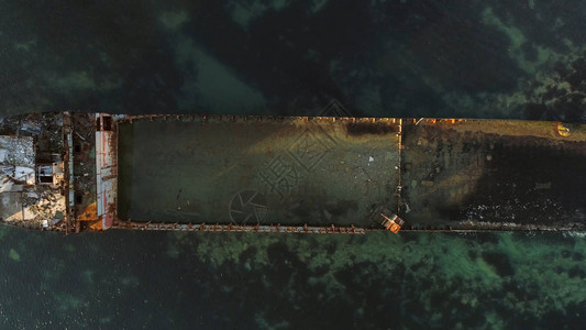 在蓝色的海水中沿着岩石海岸的失事船的空中俯视图靠近海边的旧沉图片