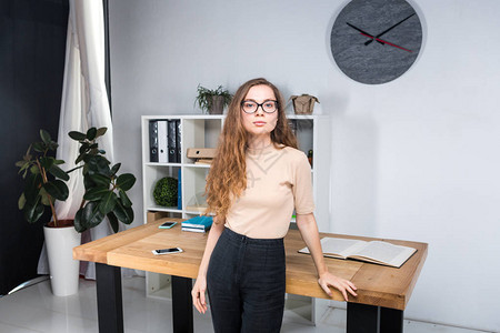 一位留着长发和戴眼镜的年轻白人女肖像站在办公桌附近的办公室内女大学生图片