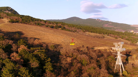 黄色索道的空中与在树坡背景上移动电缆铁路在日落时分越过森图片