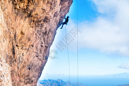 攀岩者爬上悬垂的悬崖背景是山脉和大海图片