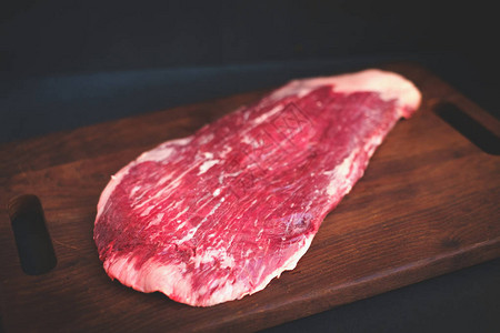 肉店黑色背景的木板上未煮熟的侧腹牛排图片