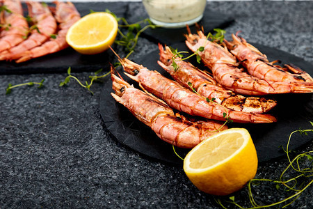 黑石板上的烤大虎虾配香料柠檬黑色背景的新鲜香草顶视图烤海鲜烤图片