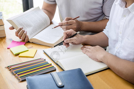 高中导师或大学生群体坐在图书馆的办公桌前学习和阅读图片