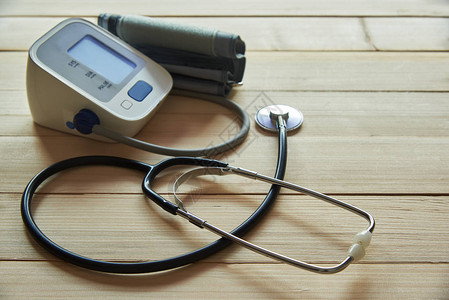 木制背景上的黑色听诊器和数字血压计图片