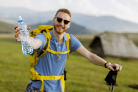 年轻英俊的徒步旅行者停下来喝了一瓶水图片