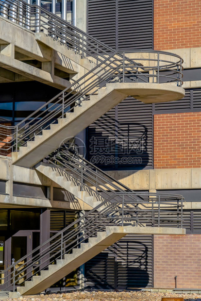 在阳光明媚的日子里观看的建筑物的室外楼梯带有半圆形平台和金属扶手的L形楼梯的建筑物飞行在阳光明媚的日子里图片