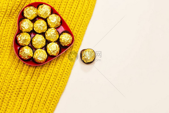 羊毛芥末色围巾上方的金色高级巧克力糖果心形盒图片