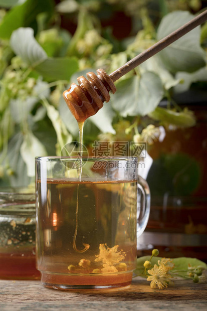 杯椴树茶蜂蜜和木桌上的鲜花图片
