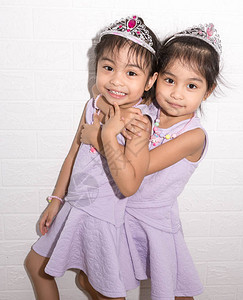 女亚洲同卵双胞胎坐在白色背景的椅子上穿着紫色的衣服和配饰站着拥图片