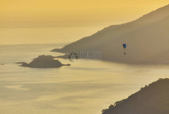 一架不明身份的滑翔伞在日落时飞越土耳其奥卢代尼兹的蓝色环图片