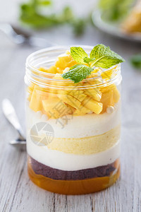 甜美的自制芒果甜点芝士蛋糕松糕浅色木质背景的玻璃罐中的老鼠图片