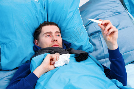 身着围巾手持温度计的病男子躺在床上图片