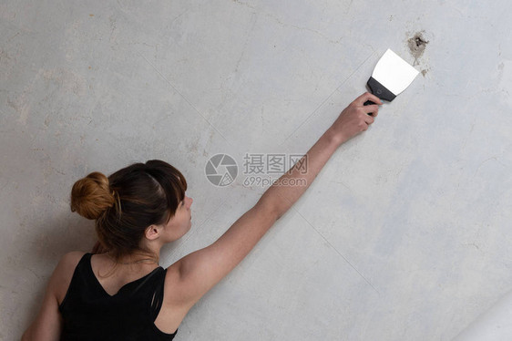 女孩修理公寓一个女人在混凝土墙上拿着一把抹刀装修公寓腻子图片
