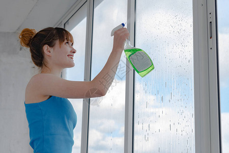 女孩在脏玻璃上喷洒液体以洗窗户图片