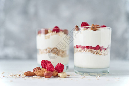 两杯希腊酸奶格兰诺拉麦片配覆盆子燕麦片和白色背景上的坚果背景图片
