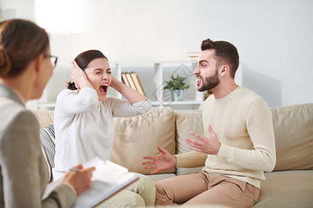 年轻烦恼的女青年在她紧张的丈夫试图在家庭聚会期间解释一些事情时图片