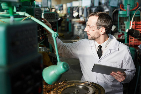 在工厂车间复印空间内穿着实验室大衣检查工业机器组的成熟主图片
