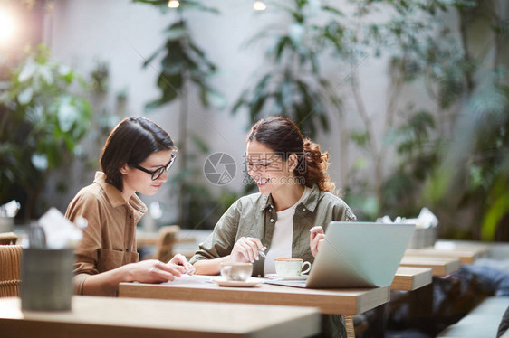 穿着休闲衬衫的快乐自信进取的女士坐在现代咖啡馆的餐桌旁图片