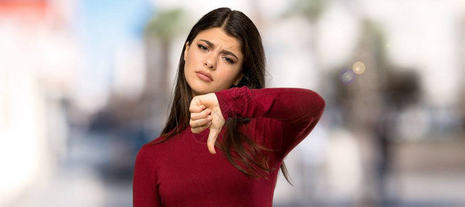 穿着高领毛衣的少女在户外用负面表情露出拇指图片