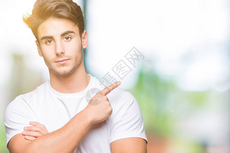 身穿白色T恤的年轻帅哥在孤立的背景下用手指着侧面展示广告图片