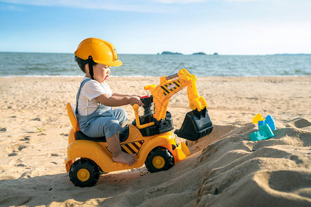 亚洲男孩在沙滩上玩挖土机玩具图片