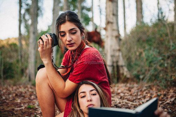 年轻一对身穿洋装看书的年轻女子在森林里用旧相机和马拍照片图片