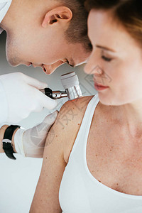 皮肤科医生在检查黑色素瘤患者时手持皮肤镜图片