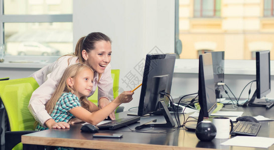 母亲和女儿正在学习课程在妈办公室上班女教师和女孩一起坐在电脑显示器旁图片