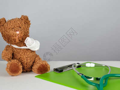 在白色背景泰迪熊旁边的医学听诊镜和绿纸持有者图片