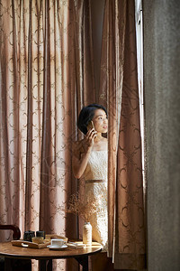 身着漂亮裙子站在窗户边看窗外的越南女青年女士图片