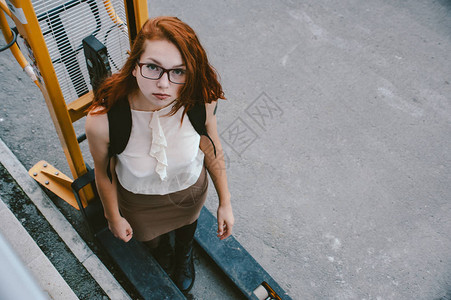 身着轻衣服和红发的女孩站在一个液压堆叠机上工图片