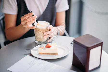 女人喝咖啡和吃蛋糕在茶餐厅的桌边图片
