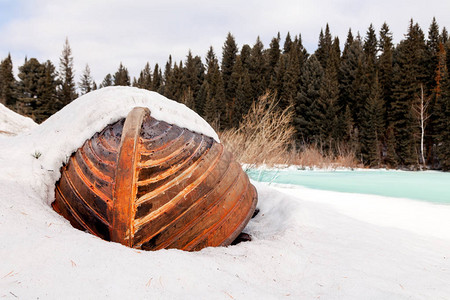 被毁坏的老木头淹水渔船位于冬季森林中冰封冷冻河岸上的雪上图片