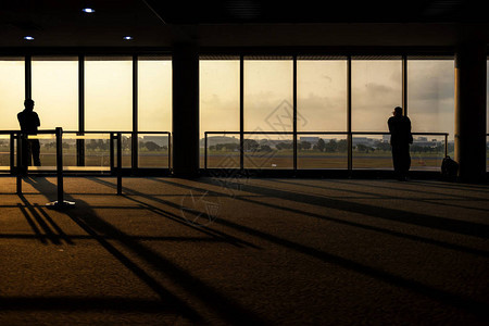 剪影旅游人或商人在日出时在靠近窗户的航站楼门口等待登机图片