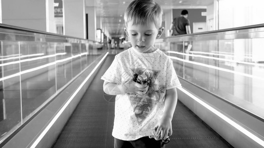 在国际机场终点站乘坐扶梯的幼儿男孩黑白肖像Blackand图片