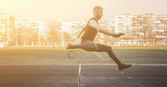 一名高加索男子跳过障碍物在体育场上奔跑田径运动员在飞行中穿着运动服精力充沛的体育活动户外运动背景图片